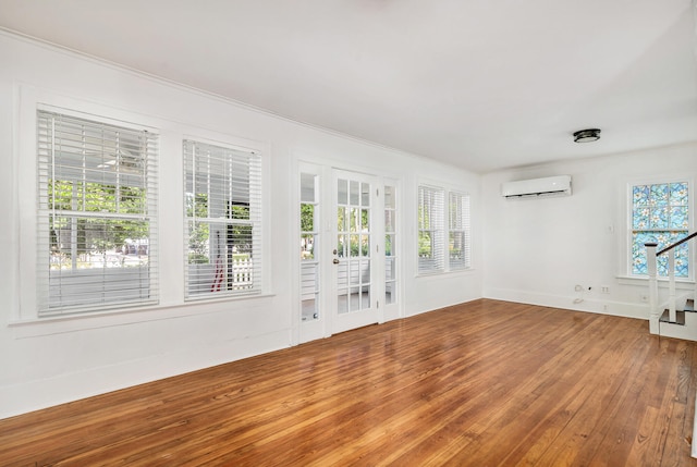 empty room with hardwood / wood-style flooring, crown molding, a wall mounted air conditioner, and a healthy amount of sunlight