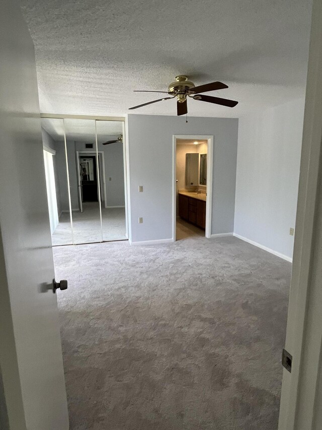 unfurnished bedroom with a textured ceiling, a closet, ensuite bathroom, light colored carpet, and ceiling fan