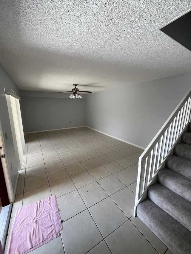 interior space with baseboards, ceiling fan, stairway, tile patterned floors, and a textured ceiling