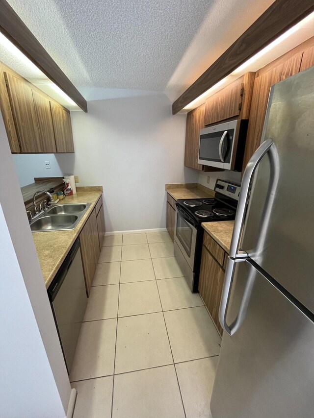 kitchen with a textured ceiling, light tile patterned flooring, stainless steel appliances, and sink