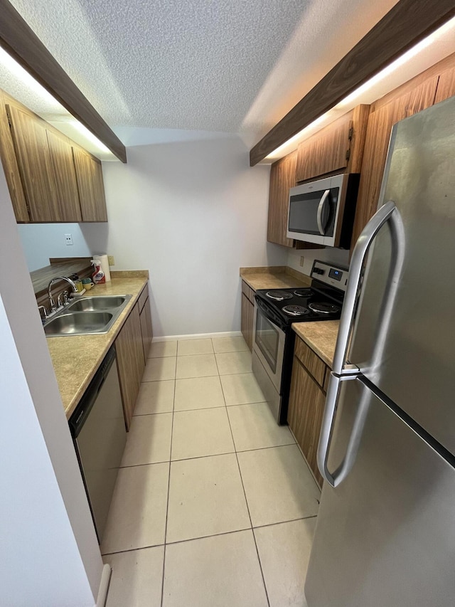 kitchen with light tile patterned flooring, a sink, light countertops, appliances with stainless steel finishes, and brown cabinets