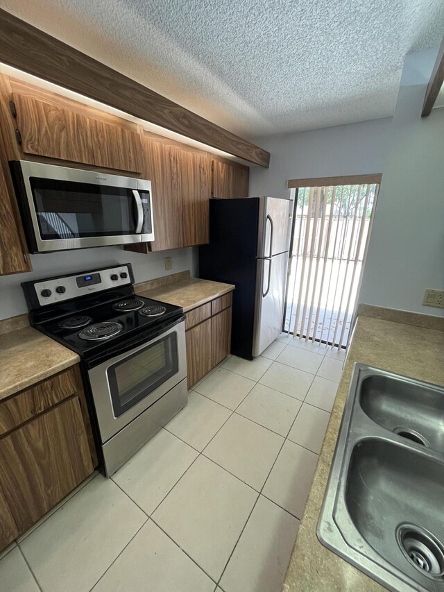 kitchen with light tile patterned floors, stainless steel appliances, sink, and a textured ceiling