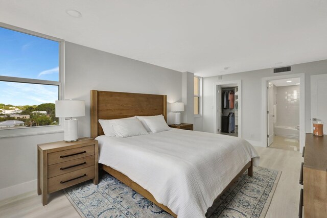 bedroom with a walk in closet, a closet, ensuite bathroom, and light hardwood / wood-style flooring