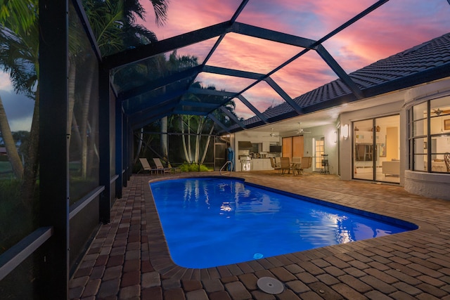 pool at dusk with glass enclosure, ceiling fan, and a patio area