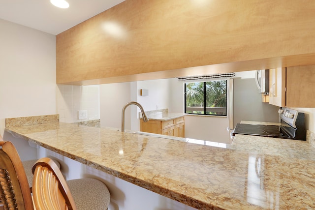 kitchen featuring a kitchen bar, kitchen peninsula, electric stove, and light brown cabinets