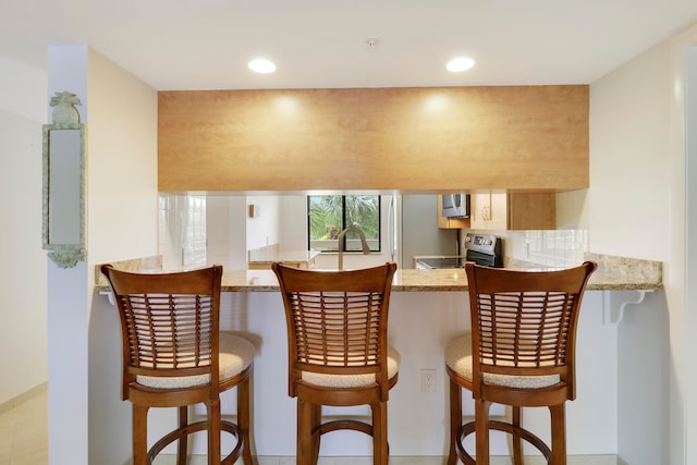 kitchen with light stone countertops, a kitchen bar, kitchen peninsula, and appliances with stainless steel finishes