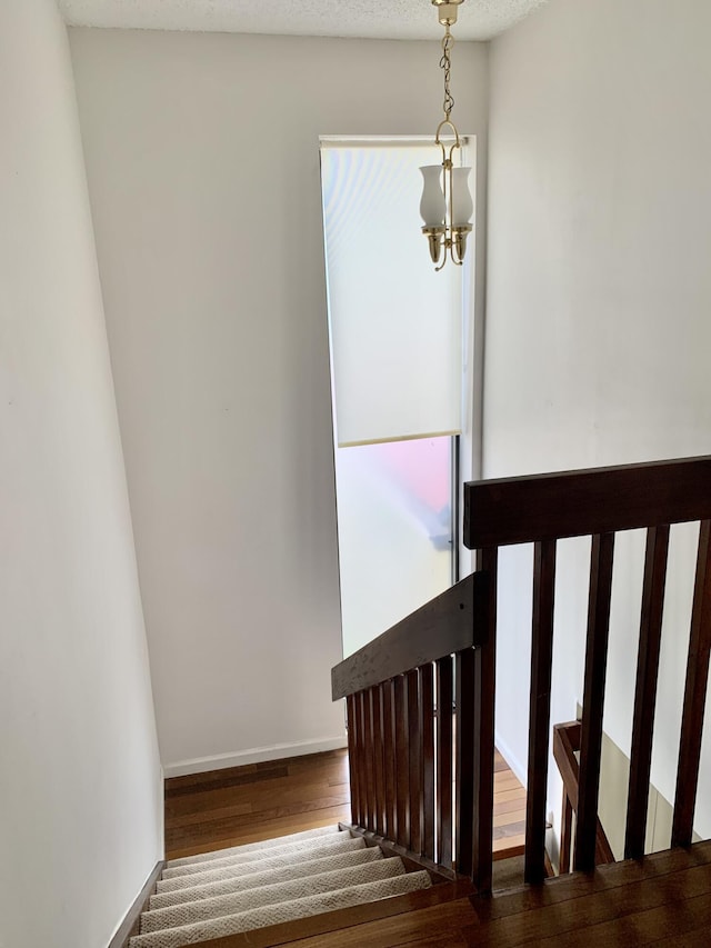 stairs featuring baseboards, wood finished floors, and an inviting chandelier