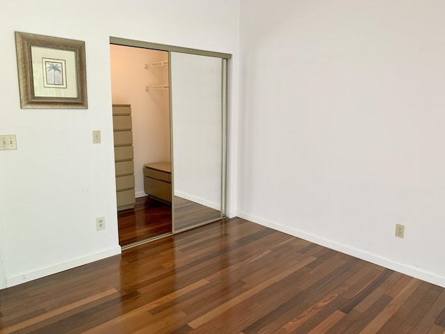 unfurnished bedroom with dark wood-style floors, baseboards, and a closet