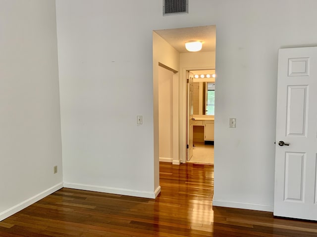 hallway with dark wood-style floors, visible vents, and baseboards