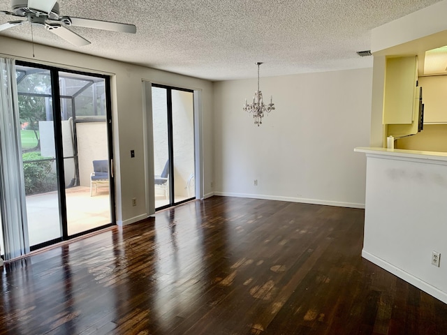 spare room featuring ceiling fan with notable chandelier, a textured ceiling, dark wood finished floors, and baseboards