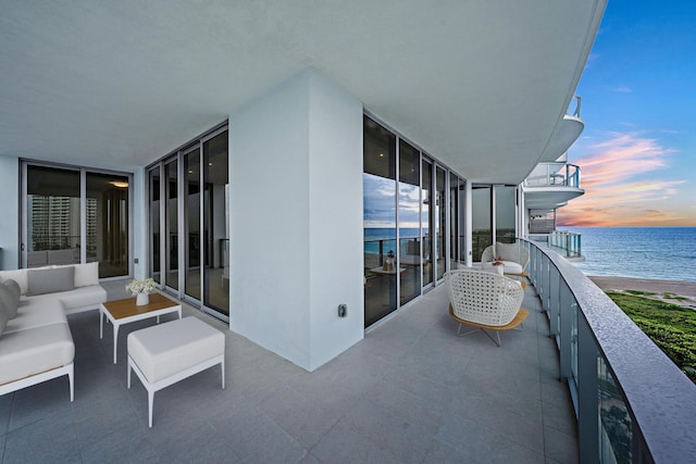 balcony at dusk with a water view, outdoor lounge area, and a view of the beach