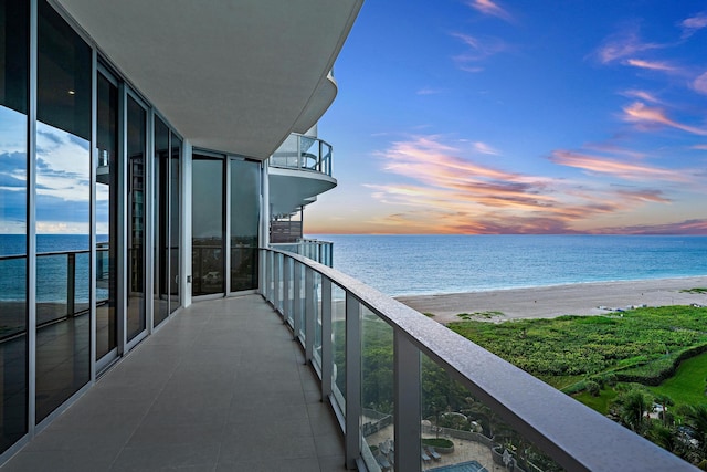 balcony at dusk with a water view and a view of the beach