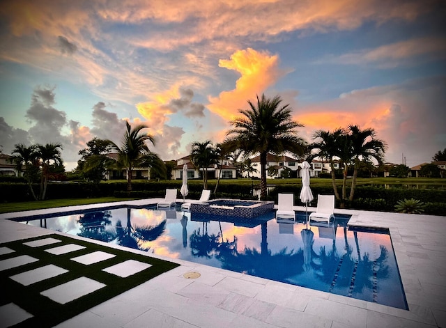 pool at dusk with a patio and an in ground hot tub