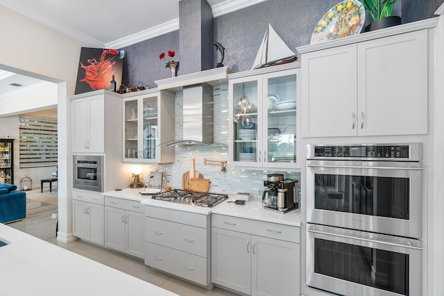 kitchen with stainless steel appliances, ornamental molding, decorative backsplash, wall chimney exhaust hood, and white cabinets