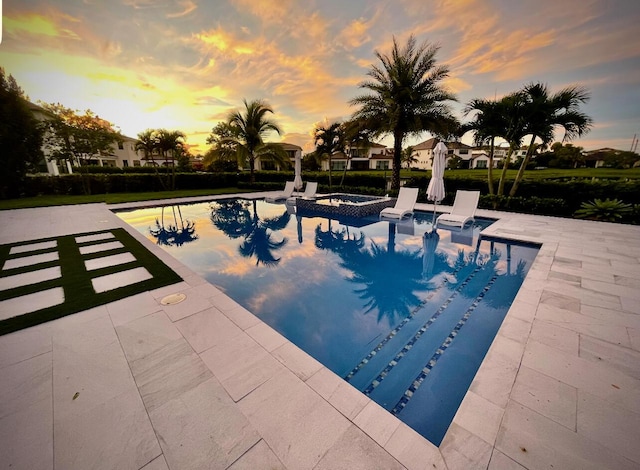 pool at dusk with an in ground hot tub and a patio area