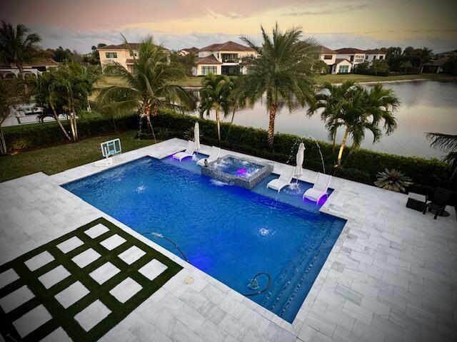 pool at dusk with a patio area, pool water feature, and an in ground hot tub