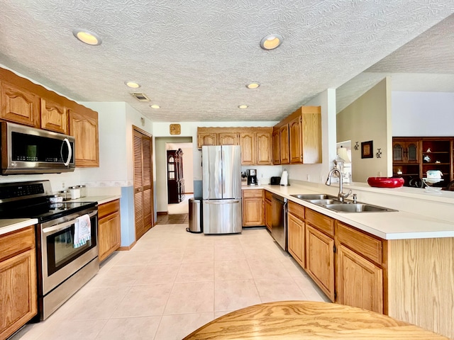 kitchen with light tile patterned floors, appliances with stainless steel finishes, sink, kitchen peninsula, and a textured ceiling