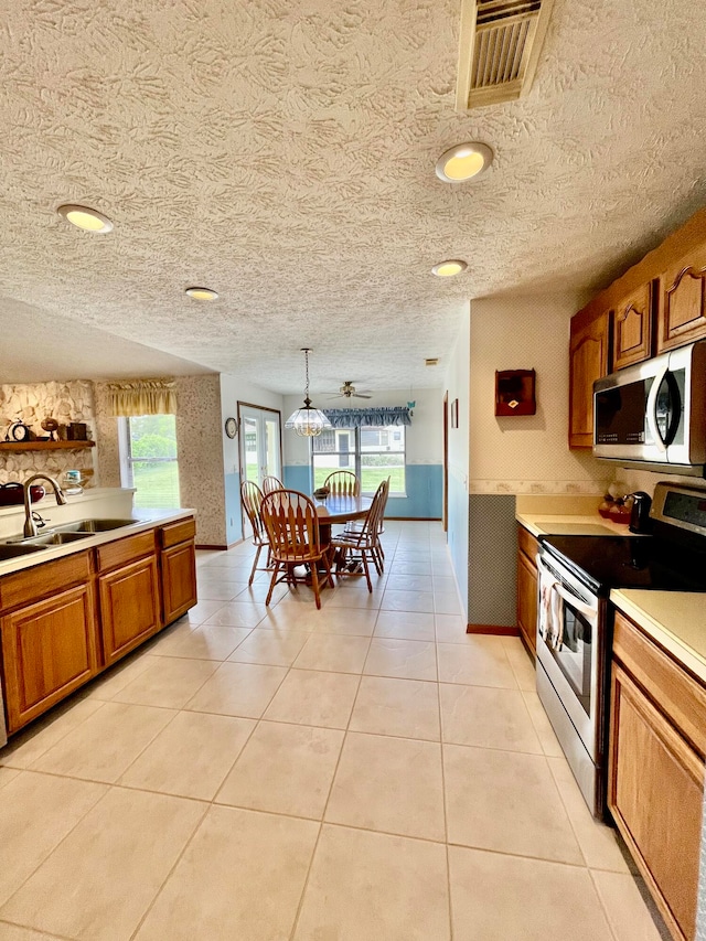 kitchen with pendant lighting, a textured ceiling, stainless steel appliances, sink, and light tile patterned flooring