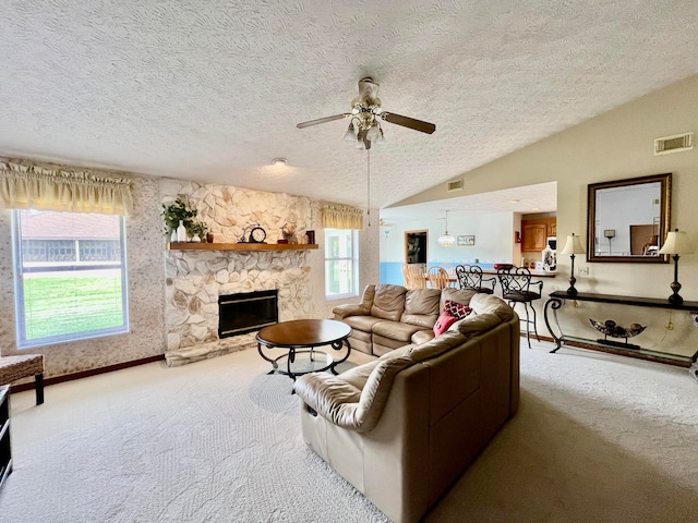 carpeted living room featuring a textured ceiling, ceiling fan, a stone fireplace, and vaulted ceiling