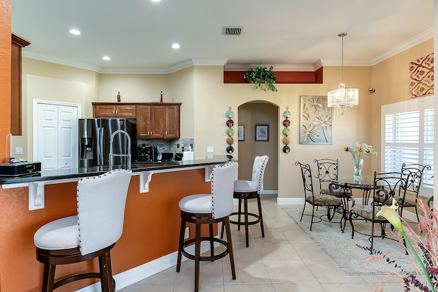 kitchen with light tile patterned floors, kitchen peninsula, decorative light fixtures, stainless steel refrigerator with ice dispenser, and a kitchen bar