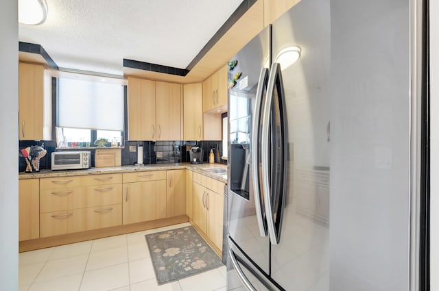 kitchen with tasteful backsplash, light tile patterned floors, light brown cabinetry, light stone countertops, and stainless steel refrigerator with ice dispenser