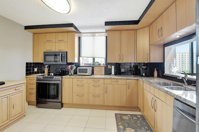 kitchen featuring appliances with stainless steel finishes, decorative backsplash, light brown cabinetry, and sink