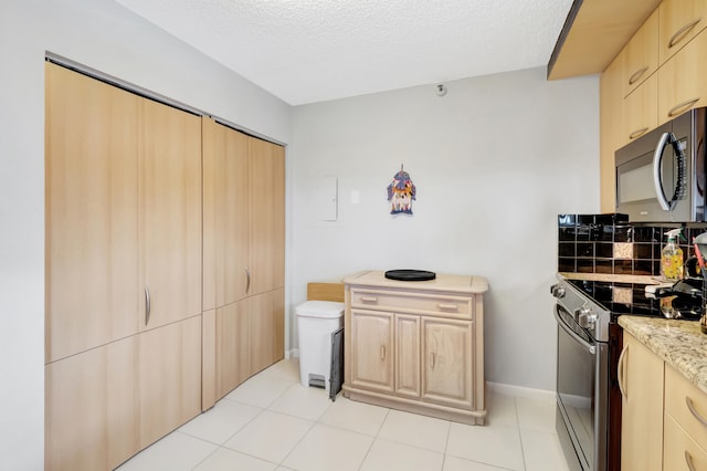 kitchen with a textured ceiling, stainless steel appliances, light tile patterned floors, and light brown cabinetry