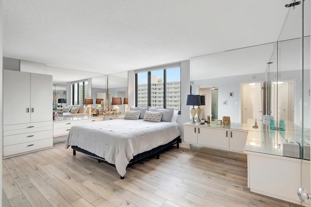 bedroom with a textured ceiling, floor to ceiling windows, and light wood-type flooring