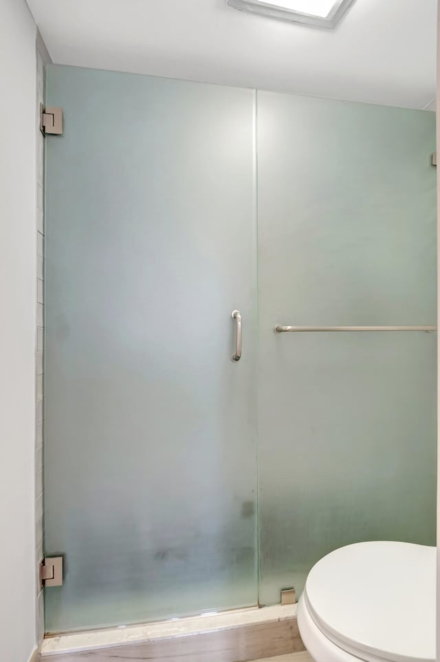 bathroom featuring a shower with door and toilet