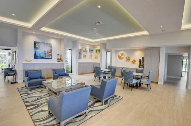 living room featuring light wood-type flooring, a tray ceiling, plenty of natural light, and ceiling fan