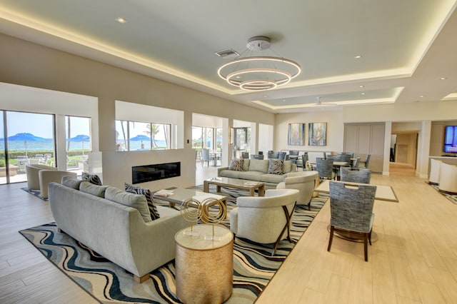 interior space with a wealth of natural light, a raised ceiling, a notable chandelier, and light hardwood / wood-style flooring