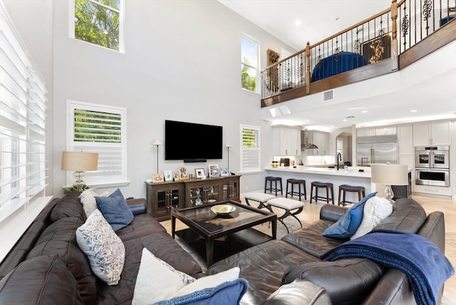 living room with a towering ceiling, light wood-style floors, visible vents, and a wealth of natural light