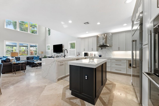 kitchen with visible vents, open floor plan, a center island, and wall chimney range hood