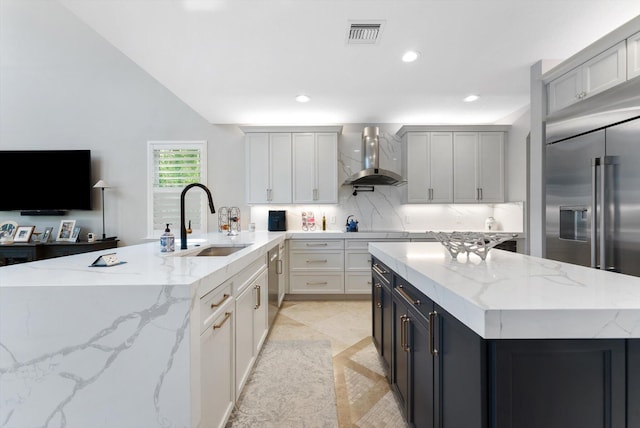 kitchen featuring visible vents, a center island, wall chimney range hood, decorative backsplash, and a sink