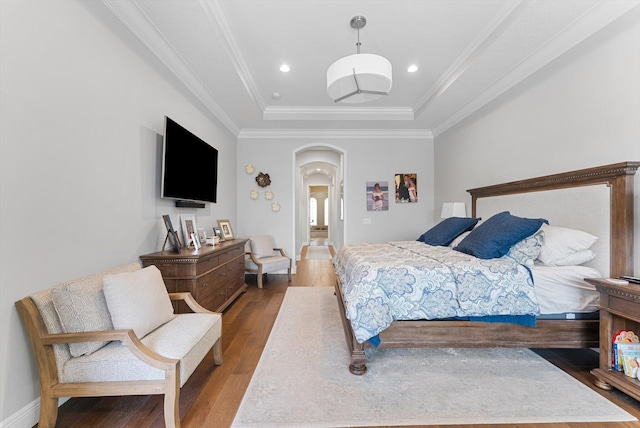 bedroom featuring a raised ceiling, ornamental molding, wood finished floors, arched walkways, and baseboards