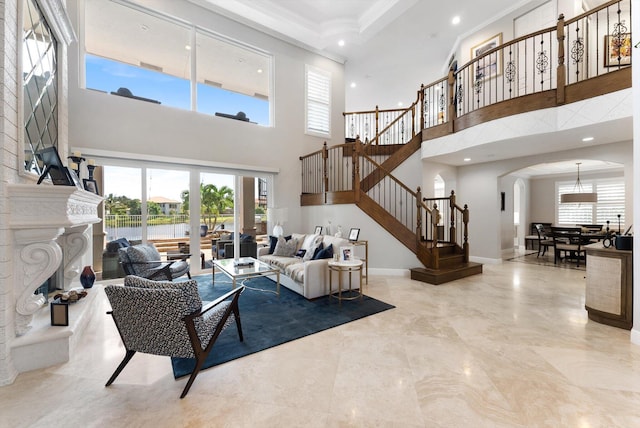 living room with ornamental molding, arched walkways, a fireplace, baseboards, and stairs