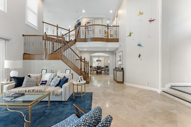 living room featuring stairs, baseboards, arched walkways, and a towering ceiling