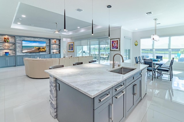 kitchen featuring visible vents, a tray ceiling, ornamental molding, gray cabinetry, and a sink