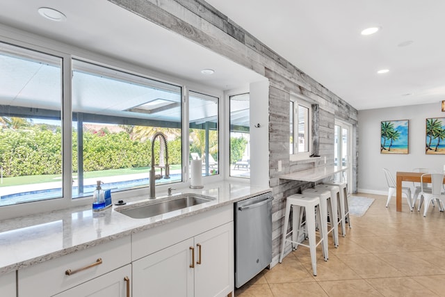 kitchen with light stone counters, white cabinetry, sink, light tile patterned flooring, and stainless steel dishwasher