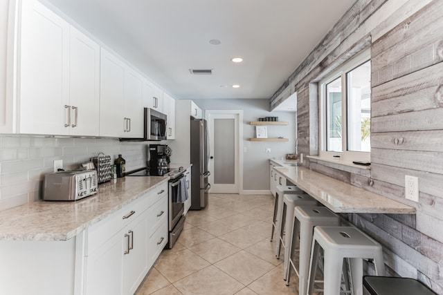 kitchen with appliances with stainless steel finishes, light stone countertops, white cabinets, and decorative backsplash