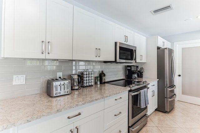 kitchen with light tile patterned floors, stainless steel appliances, decorative backsplash, light stone counters, and white cabinets