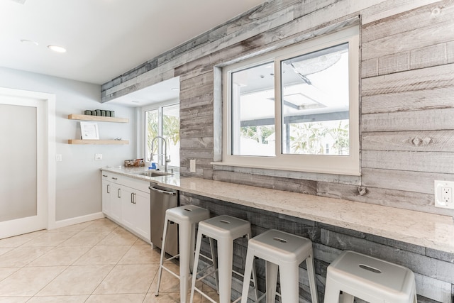 kitchen with light tile patterned floors, stainless steel dishwasher, sink, white cabinetry, and light stone counters