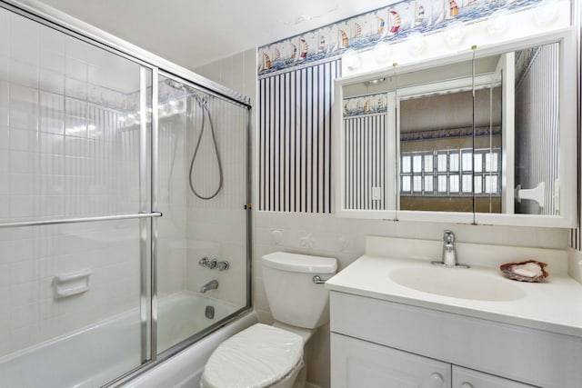 full bathroom with vanity, toilet, bath / shower combo with glass door, and tile walls