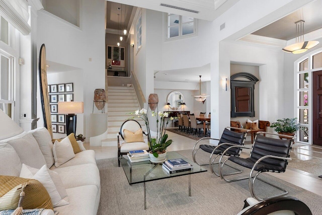 living area with visible vents, crown molding, stairway, and a towering ceiling