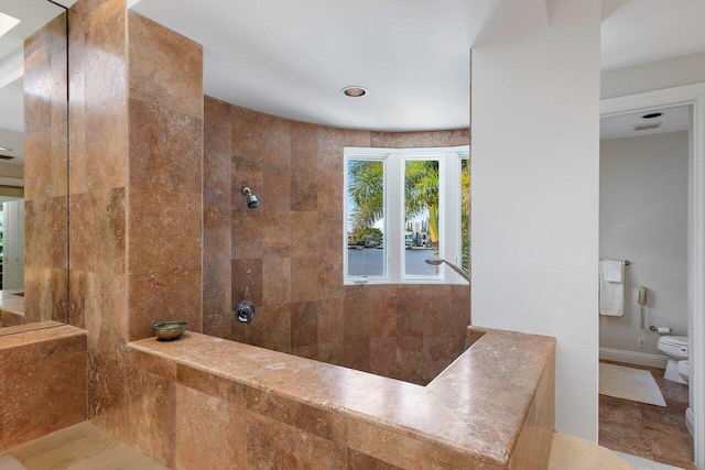 bathroom with tiled shower, toilet, and tile patterned flooring