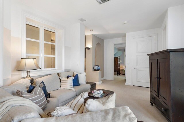 living area featuring light carpet, baseboards, visible vents, and arched walkways