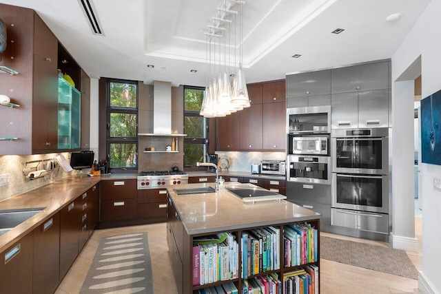 kitchen featuring a center island with sink, decorative backsplash, a raised ceiling, and sink