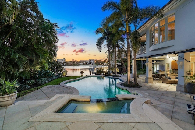 pool at dusk featuring an in ground hot tub, a patio, and a water view