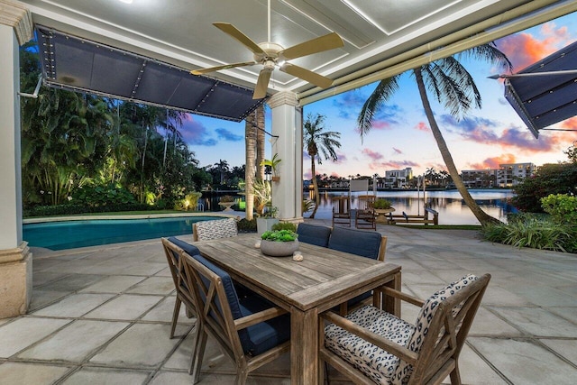 patio terrace at dusk with ceiling fan, outdoor dining area, a water view, and an outdoor pool