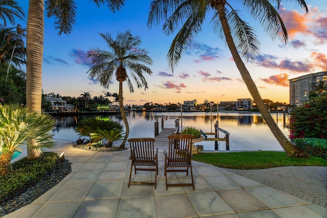 patio terrace at dusk featuring a water view, a boat dock, and boat lift